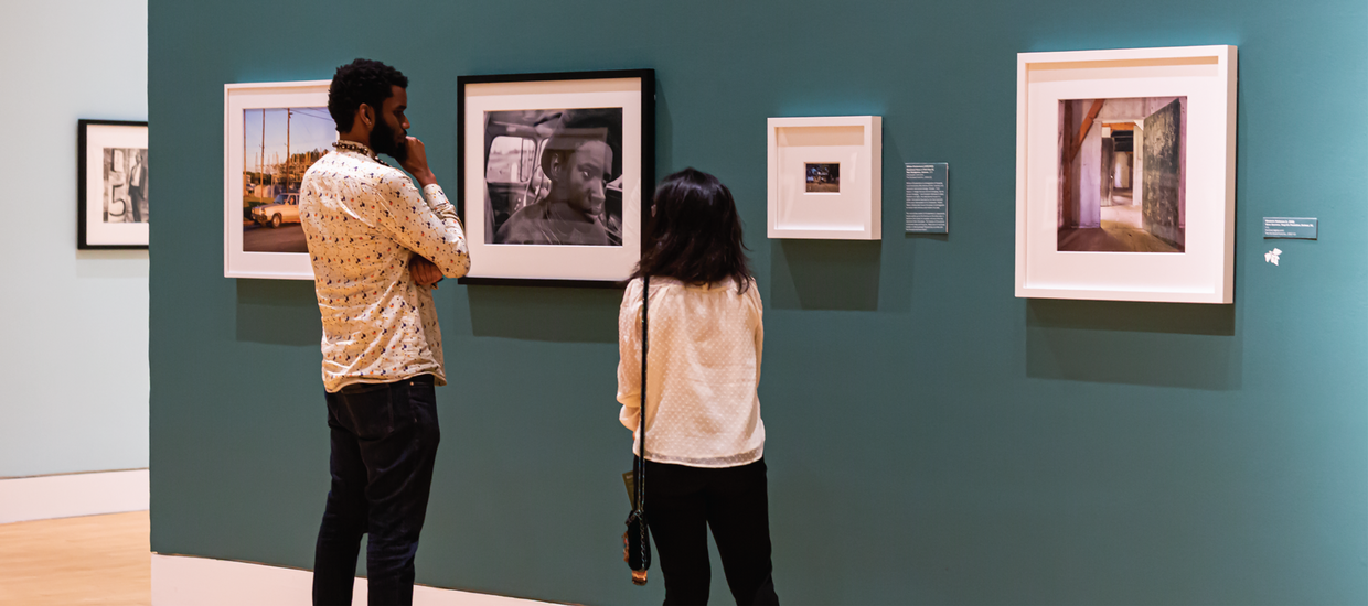 Two people standing in a gallery with four photographs on the wall